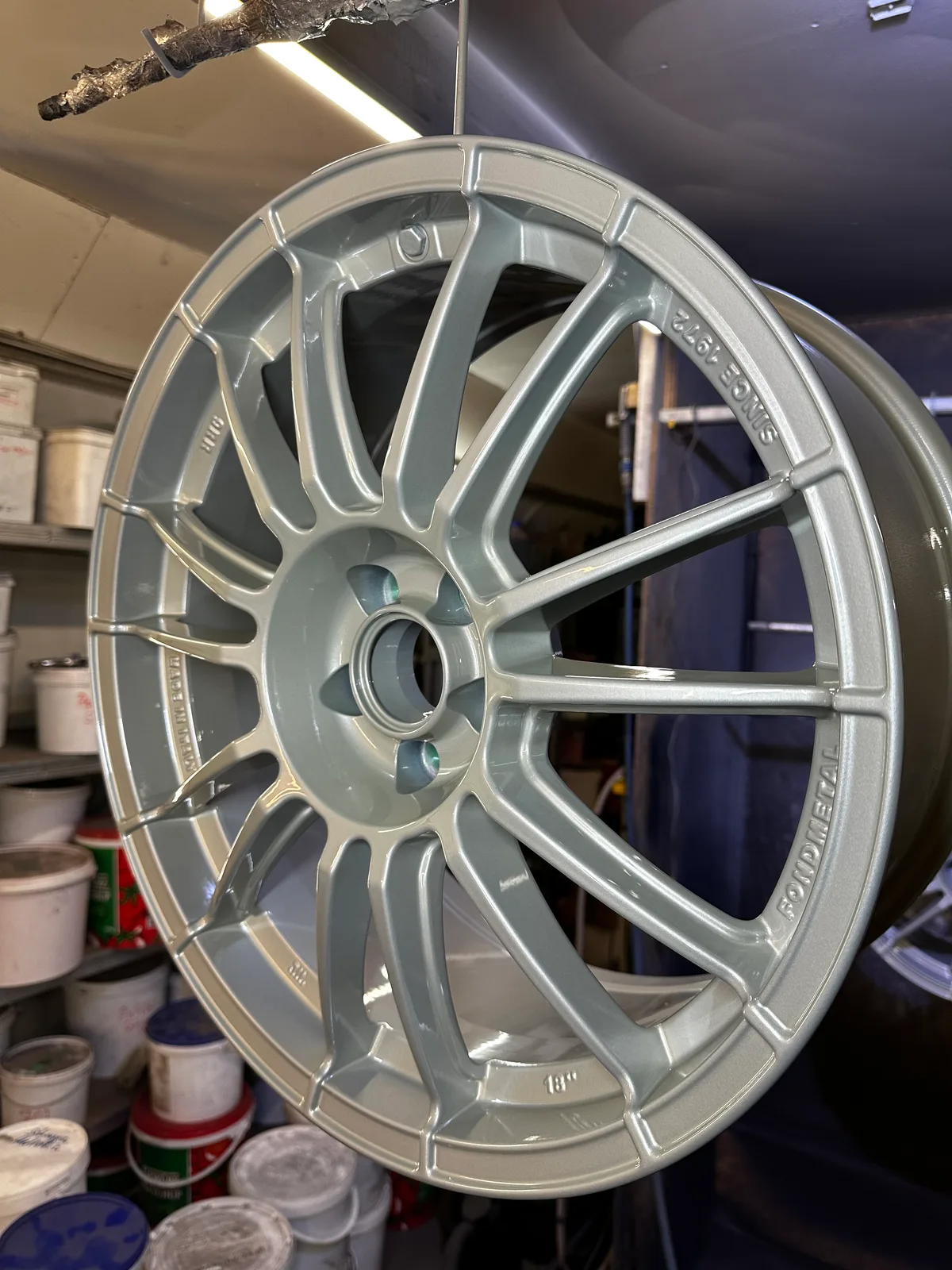 Hellgrau-mintfarben pulverbeschichtete Fondmetal-Rennsportfelge in 18 Zoll, hängend vor dem Farblager