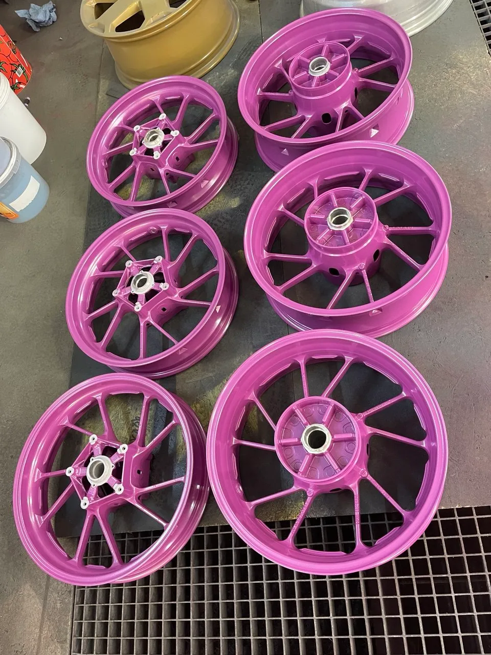 Sechs pink pulverbeschichtete Motorradfelgen in verschiedenen Größen auf dem Werkstatttisch