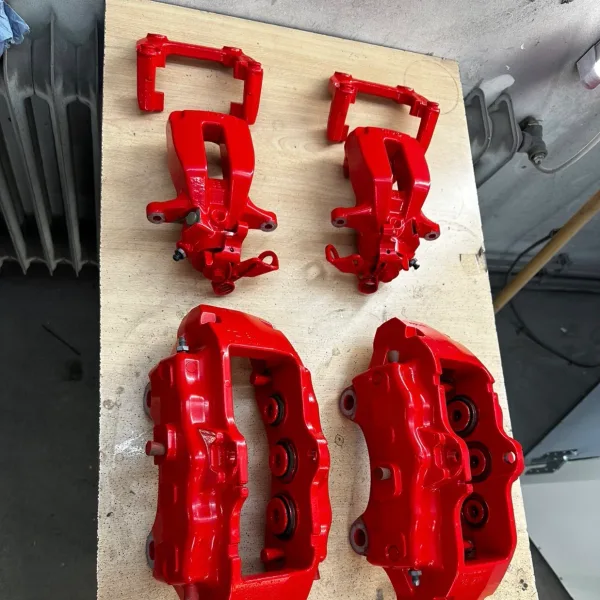 Vier leuchtend rot pulverbeschichtete Bremssättel mit Haltern auf einer Holzplatte