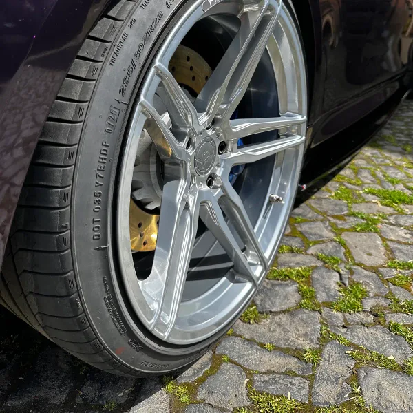 Silbern pulverbeschichtete Felge montiert an einem violetten Sportwagen, mit blauem Bremssattel und gelochter Bremsscheibe